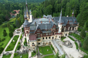 Aerial photo of Peleș Castle in Sinaia, Romania, surrounded by Carpathian forest and manicured gardens.