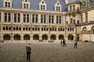Visitors in the grand courtyard of Château de Pierrefonds, ornate Gothic-Renaissance stone facades and arched galleries.
