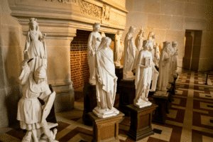 Row of white medieval statues inside Pierrefonds Castle’s Salle des Preuses, by a grand stone fireplace.
