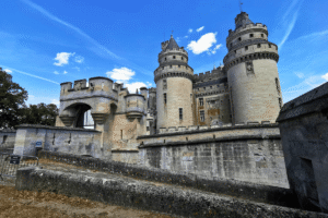 Château de Pierrefonds stone towers and gatehouse under blue sky in Oise, France.