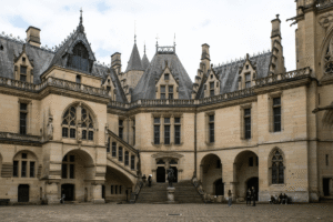 Courtyard of Château de Pierrefonds with ornate Gothic dormers, staircase, and equestrian statue.