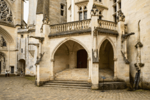 Gothic arches and staircase in Château de Pierrefonds courtyard, ornate stonework and dragon gargoyle.