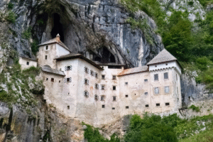 Predjama Castle built into a limestone cliff near Postojna, Slovenia, with cave entrance looming above.