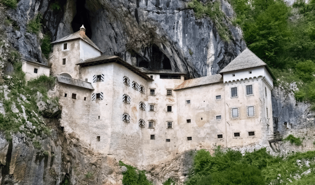 Predjama Castle built into a limestone cliff in Slovenia, with cave entrance above and green hills.