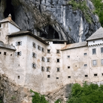 Predjama Castle built into a limestone cliff in Slovenia, with cave entrance above and green hills.
