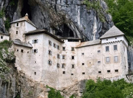 Predjama Castle built into a limestone cliff in Slovenia, with cave entrance above and green hills.