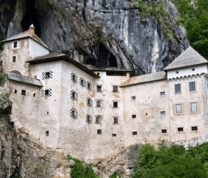 Predjama Castle built into a limestone cliff in Slovenia, with cave entrance above and green hills.