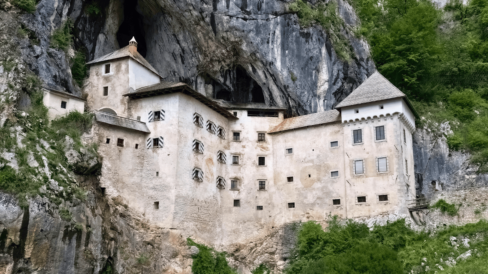 Predjama Castle built into a limestone cliff in Slovenia, with cave entrance above and green hills.