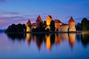 Illuminated Trakai Island Castle reflecting on Lake Galvė at blue hour in Lithuania.