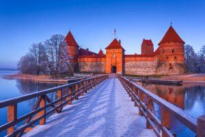 Frosty bridge leading to Trakai Island Castle over calm lake at sunrise in Lithuania