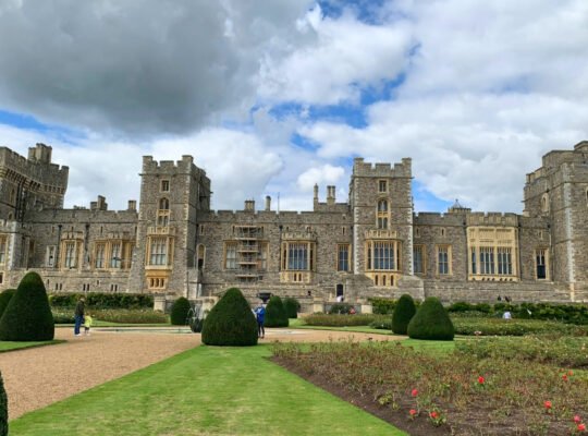 Front view of Windsor Castle with manicured gardens under cloudy sky