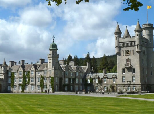 Balmoral Castle facade with turrets and manicured lawn under blue sky