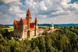 Aerial view of Bouzov Castle perched above lush forest and rolling hills