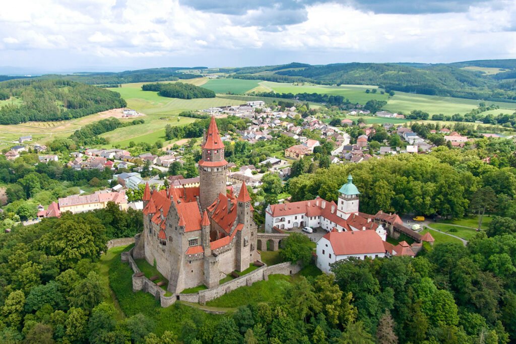 Aerial view of Bouzov Castle atop forested hill, red roofs and towers