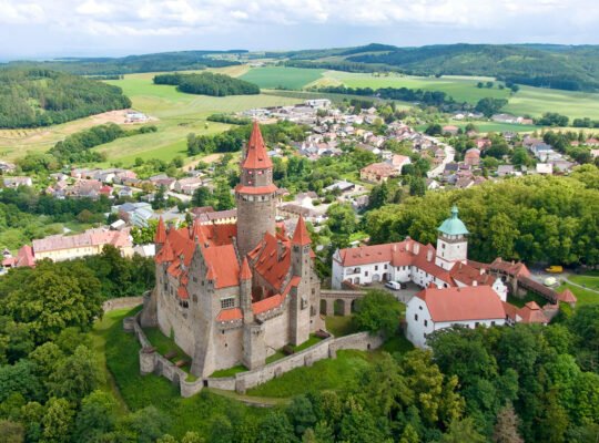 Aerial view of Bouzov Castle perched on wooded hill with red roofs