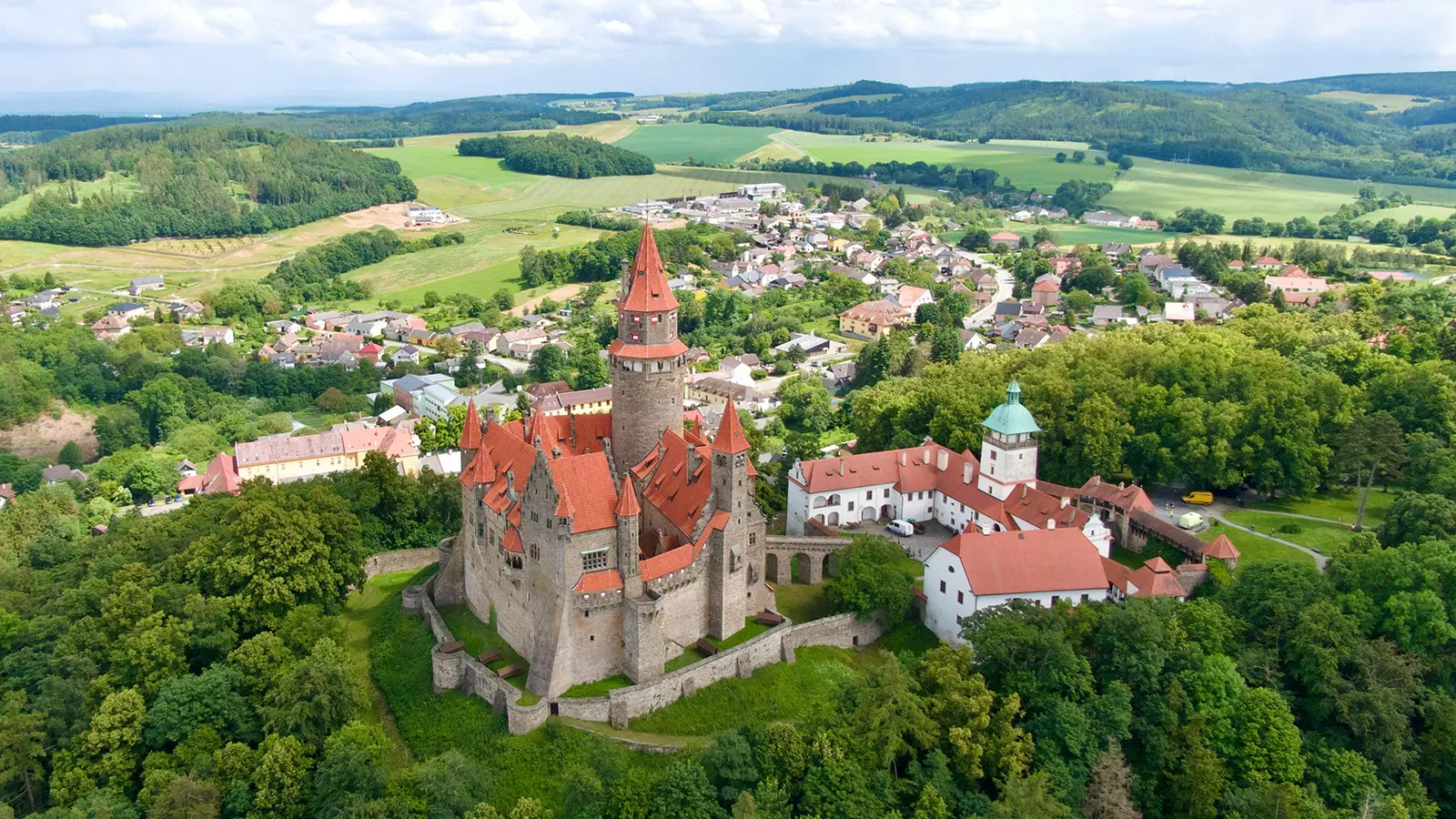 Aerial view of Bouzov Castle perched on wooded hill with red roofs