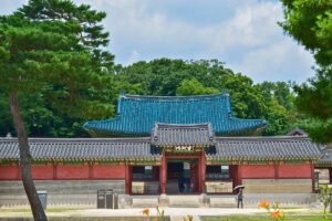 Front entrance of Changdeokgung Palace with tiled roofs, trees, and visitors under umbrellas