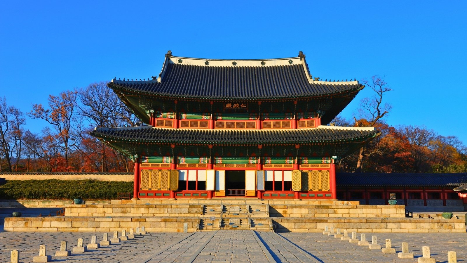 Front view of Changdeokgung Palace with autumn trees and blue sky