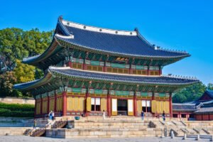 Changdeokgung Palace front facade under blue sky, visitors on stone steps