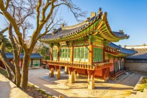 Changdeokgung Palace ornate wooden pavilion beside bare trees in golden light