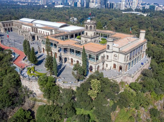 Aerial view of Chapultepec Castle perched above forested Chapultepec Park with Mexico City skyline