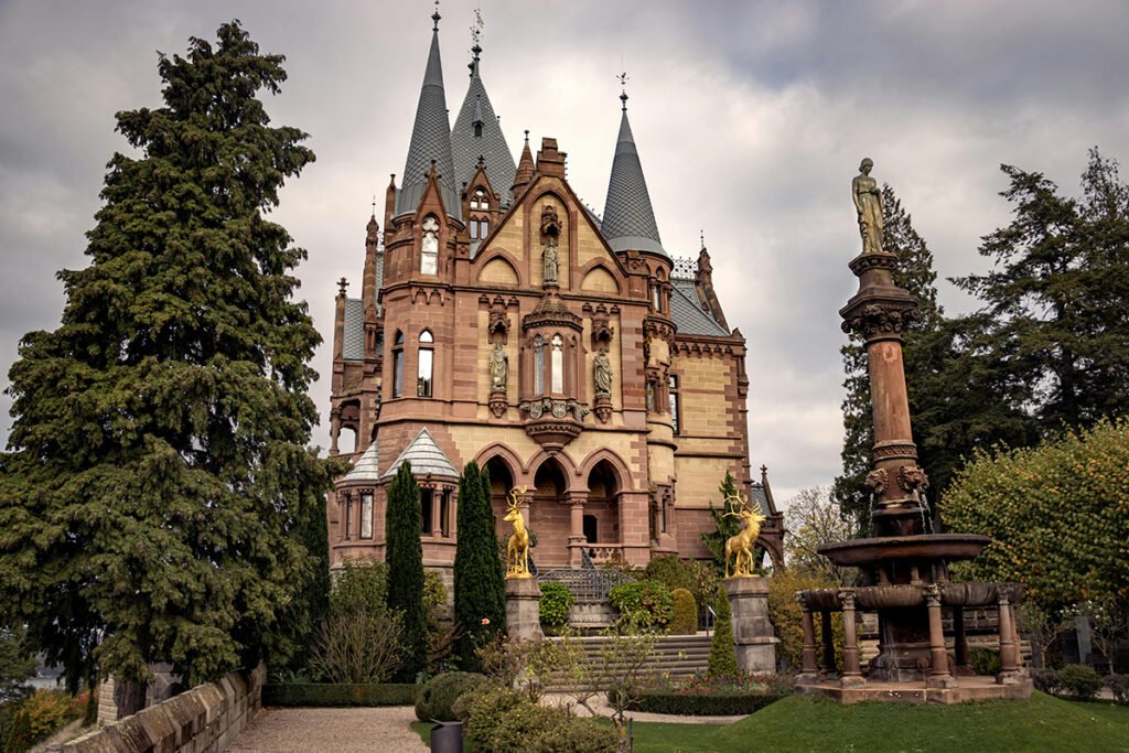 Drachenburg Castle facade with turrets and golden stag statues under cloudy sky