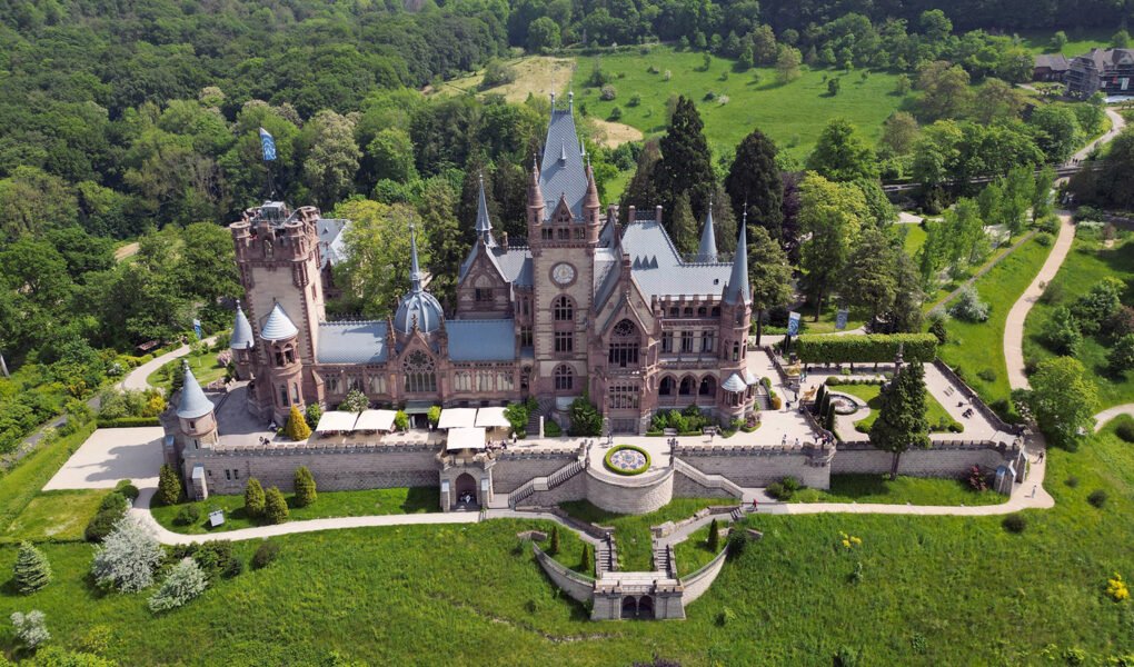 Aerial view of Drachenburg Castle surrounded by lush forest and terraces