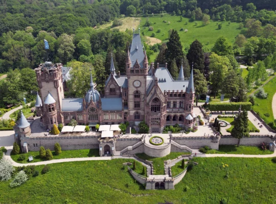 Aerial view of Drachenburg Castle surrounded by lush forest and terraces