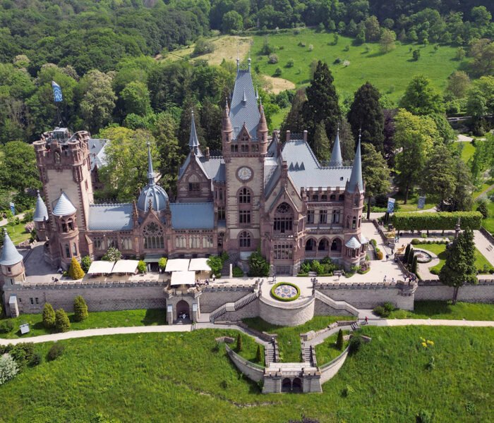 Aerial view of Drachenburg Castle surrounded by lush forest and terraces