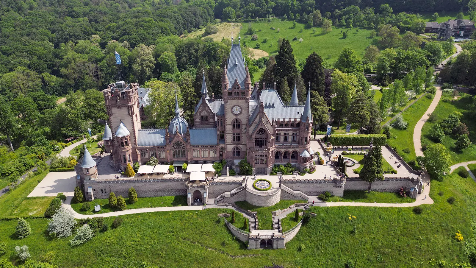 Aerial view of Drachenburg Castle surrounded by lush forest and terraces