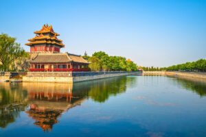 Forbidden City corner tower reflected in tranquil moat under clear blue sky