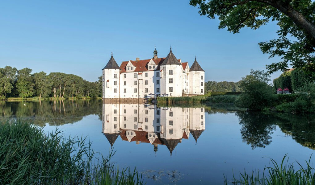 Glücksburg Castle reflected in calm lake at sunrise