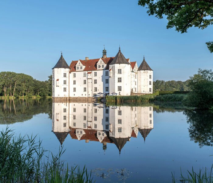 Glücksburg Castle reflected in calm lake at sunrise