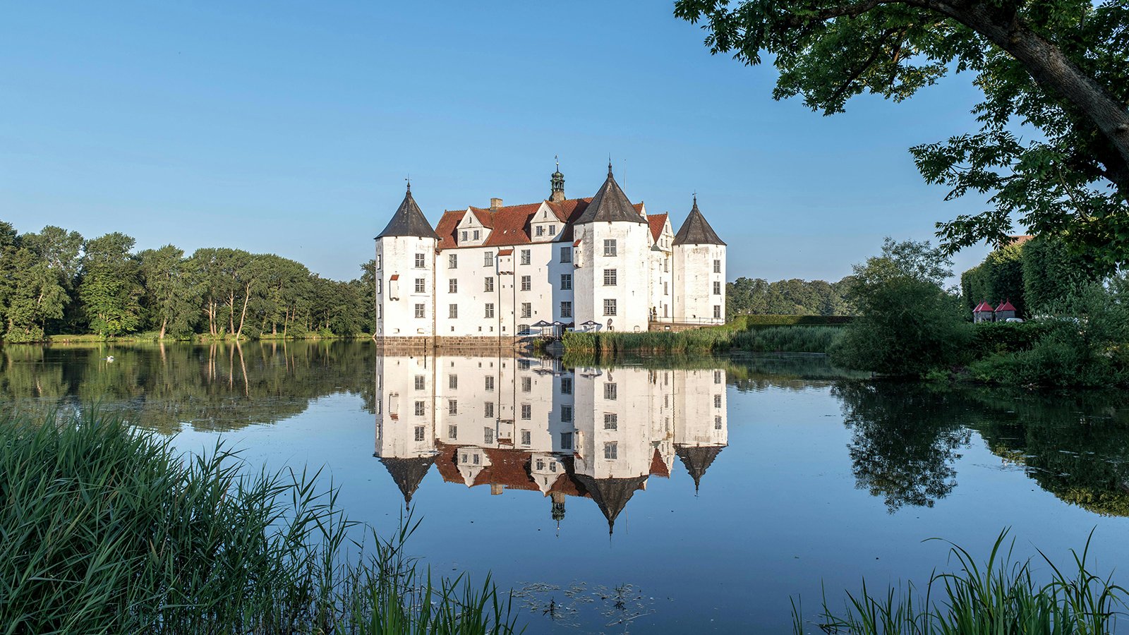 Glücksburg Castle reflected in calm lake at sunrise