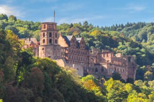 Heidelberg Castle ruins perched above forested hillside under blue sky