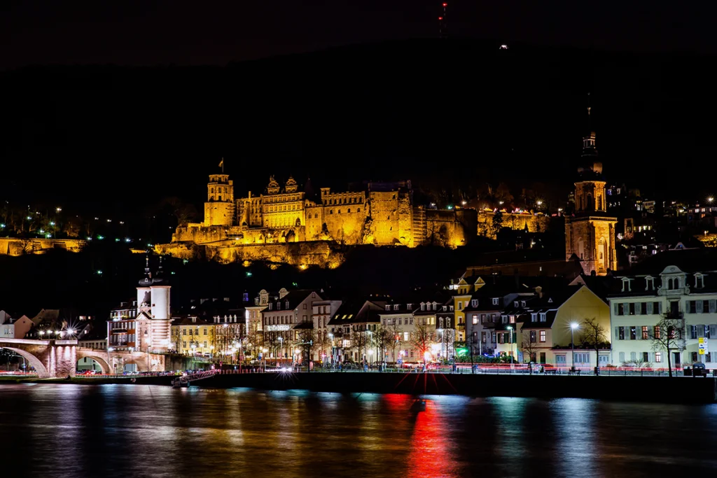 Heidelberg Castle glowing above riverside night town