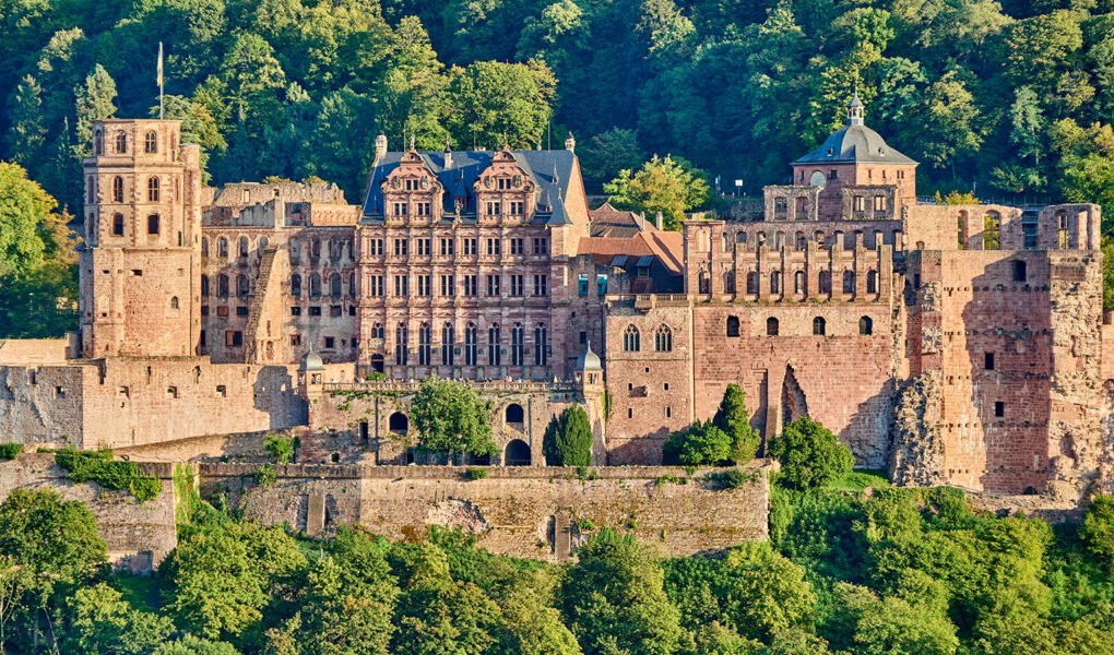 Heidelberg Castle overlooking lush forest and valley, sandstone façades in golden light