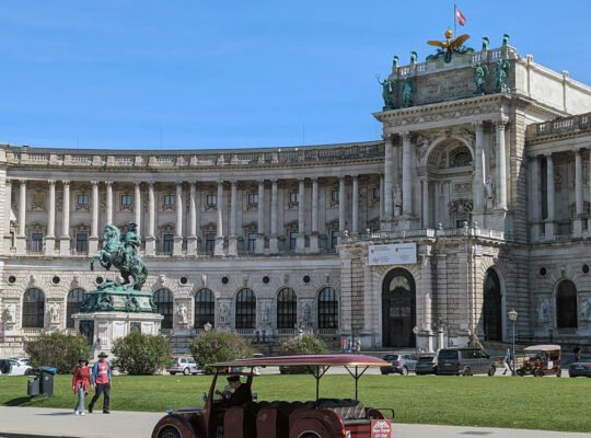 Hofburg Palace outer facade with equestrian statue and lawn under blue sky