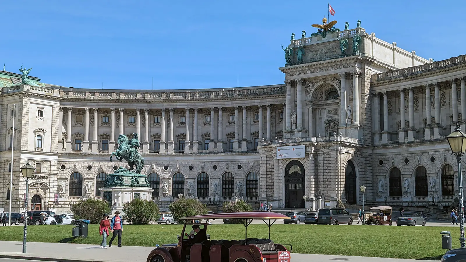 Hofburg Palace outer facade with equestrian statue and lawn under blue sky
