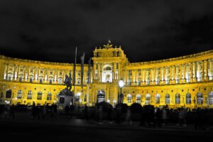 Hofburg Palace illuminated facade at night, crowds in foreground