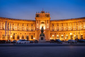 Hofburg Palace illuminated at dusk with equestrian statue in foreground