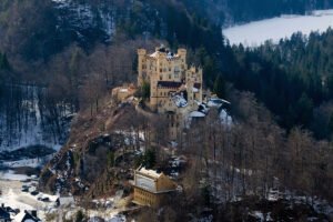 Hohenschwangau Castle perched on snowy hill surrounded by forest and lake views