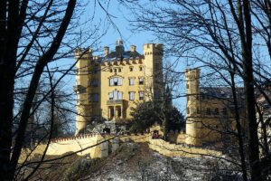Hohenschwangau Castle through bare winter trees on sunlit hilltop