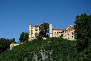 Hohenschwangau Castle atop green Bavarian hillside under blue sky