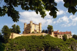 Hohenschwangau Castle perched above green cliff under blue summer sky
