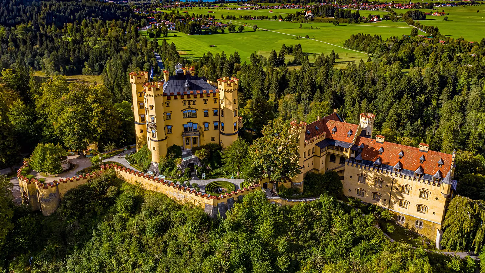 Aerial view of Hohenschwangau Castle atop wooded hill