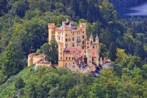 Hohenschwangau Castle perched among green forest with lake glimpsed behind