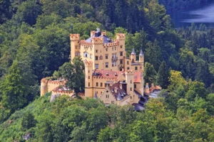 Hohenschwangau Castle perched among green forest with lake glimpsed behind