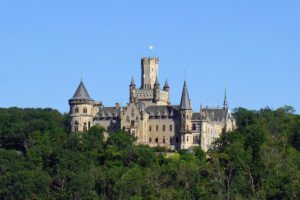 Marienburg Castle rising above dense green forest under blue sky