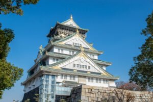 Osaka Castle white five-tiered keep framed by blue sky and trees